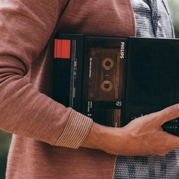 Quelqu'un dont on ne voit que le buste tient sur son bras un lecteur de cassettes portable Philips.