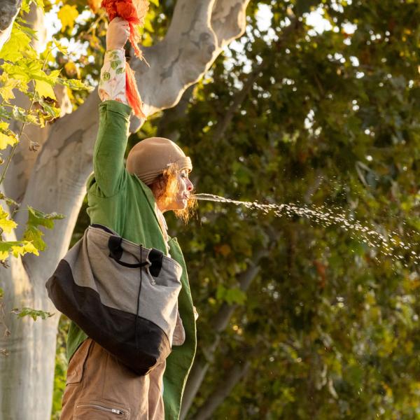 L'artiste clown est accrochée en l'air à une branche d'arbre. Elle crache de l'eau.