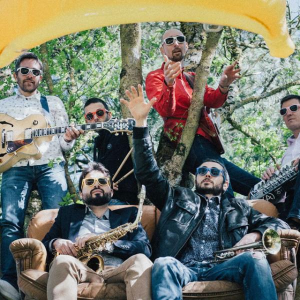 Dans un arbre, les six membres du groupes posent avec leurs instruments. Deux sont assis dans un canapé, les auyres sont debout ou posés sur des branches. Ils portent des lunettes de soleil et une banane gonflable flotte au-dessus du groupe.