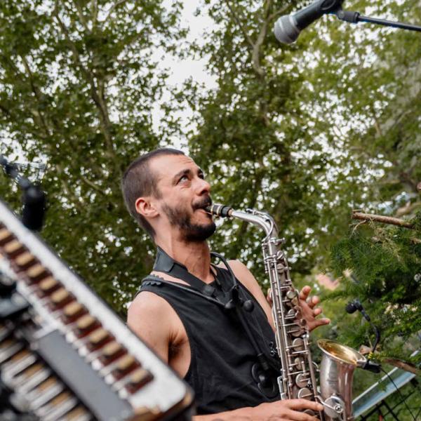 Trois musiciens en extérieur ; un joue de l'accordéon, un joue du saxophone et le dernier du darbuka.