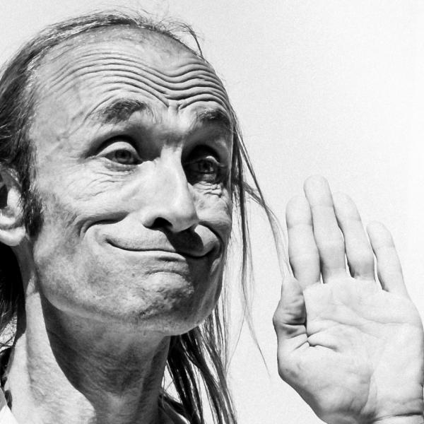 Photo en noir et blanc de Patrick de Valette, sur fond blanc. Il fait une grimace en haussant les sourcils, les mains levées.