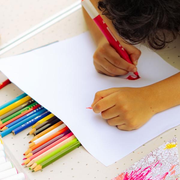 Un enfant dessine à une table. Il y a plein de crayons et de feutres.