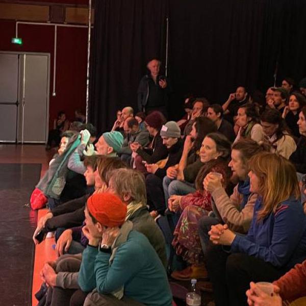 Un homme se tient debout avec un micro dans la petite salle du Kiwi devant un public au complet.