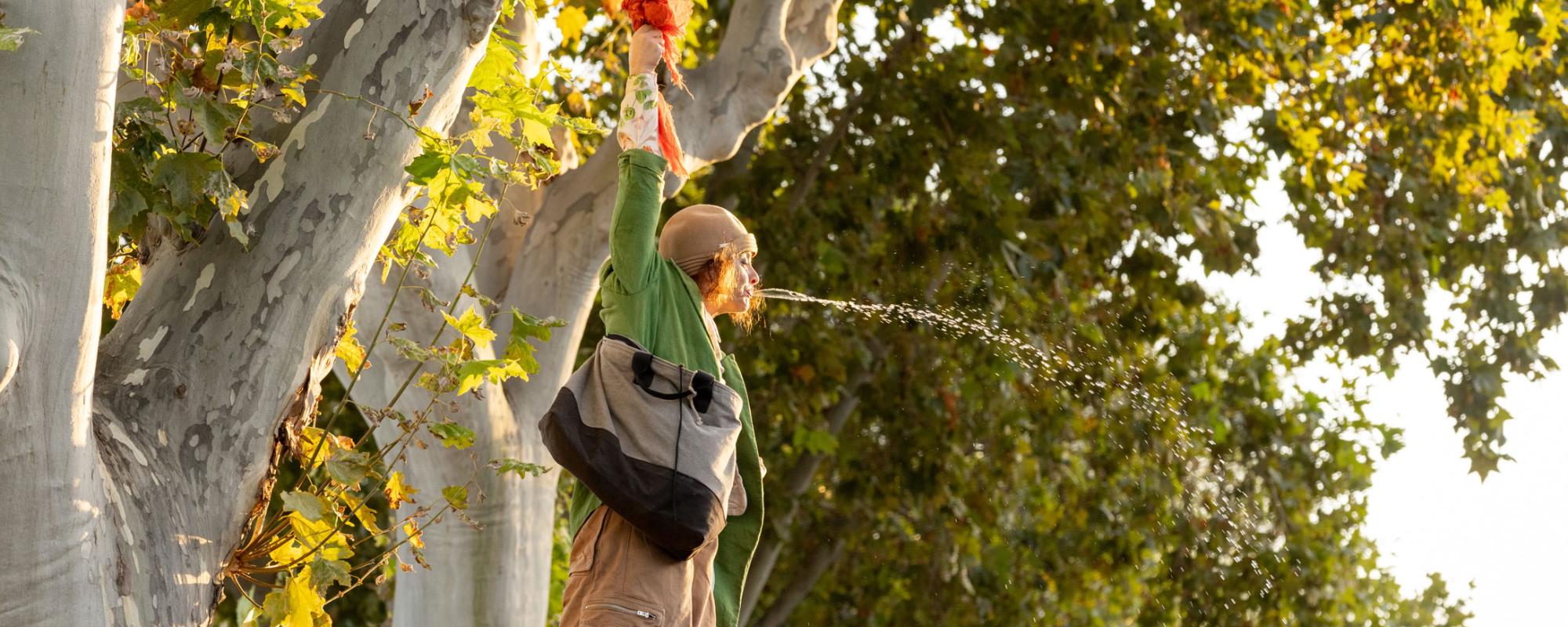 L'artiste clown est accrochée en l'air à une branche d'arbre. Elle crache de l'eau.