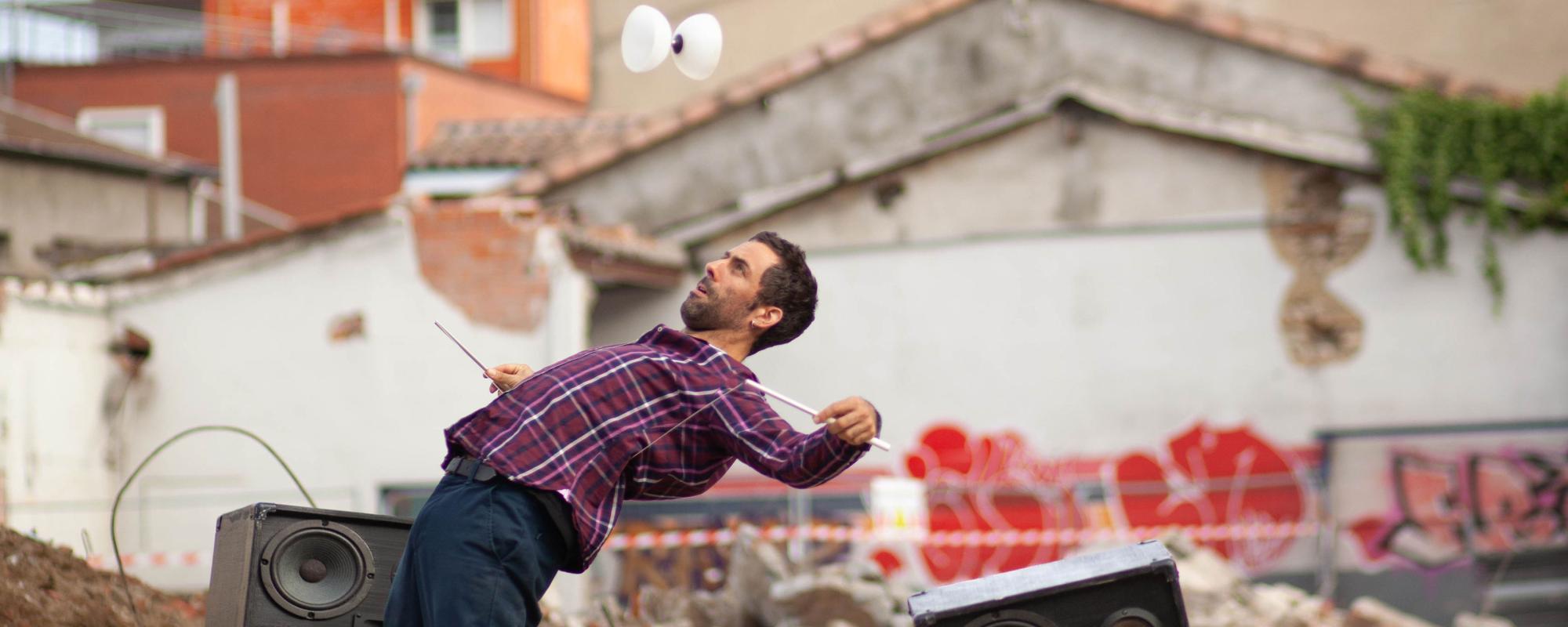 Sur un chantier d'un bâtiment démoli, l'artiste fait sauter son diabolo. Il se courbe vers l'arrière, le diabolo au-dessus de lui. Deux grosses enceintes sont posées sur les tas de gravas.