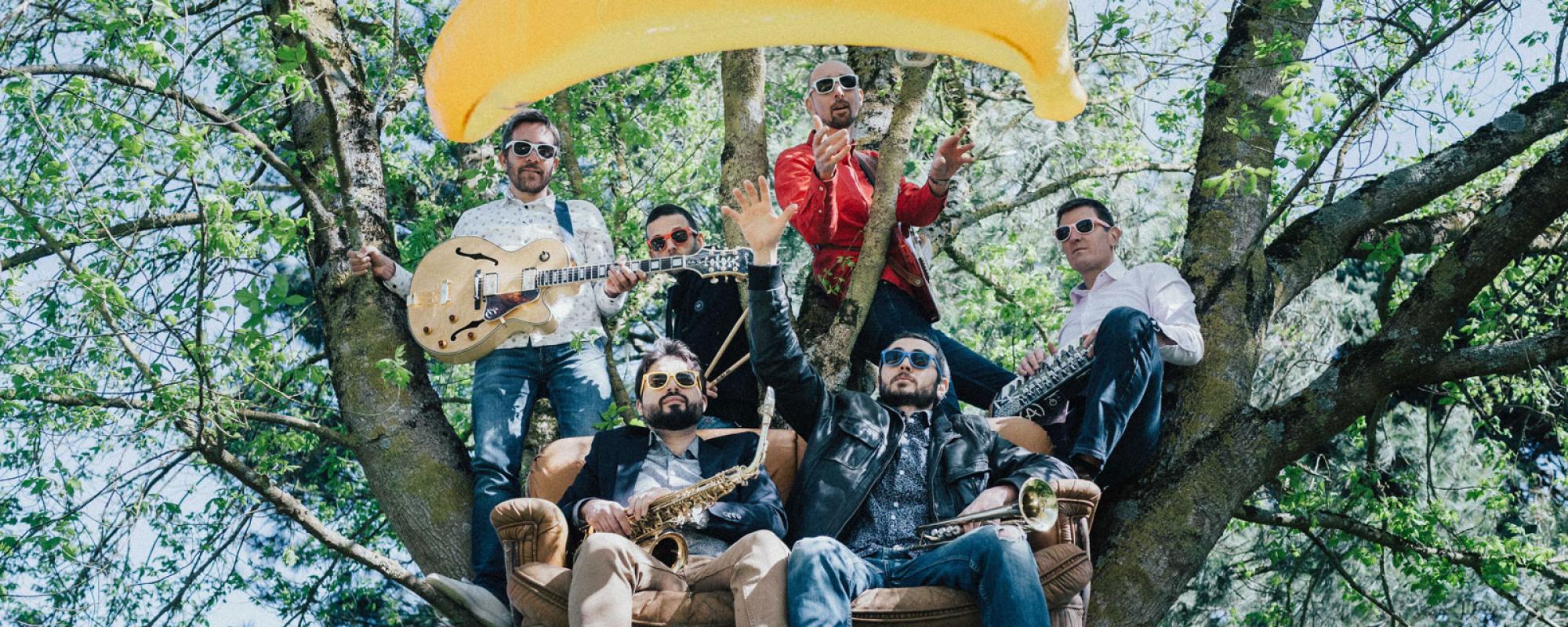 Dans un arbre, les six membres du groupes posent avec leurs instruments. Deux sont assis dans un canapé, les auyres sont debout ou posés sur des branches. Ils portent des lunettes de soleil et une banane gonflable flotte au-dessus du groupe.