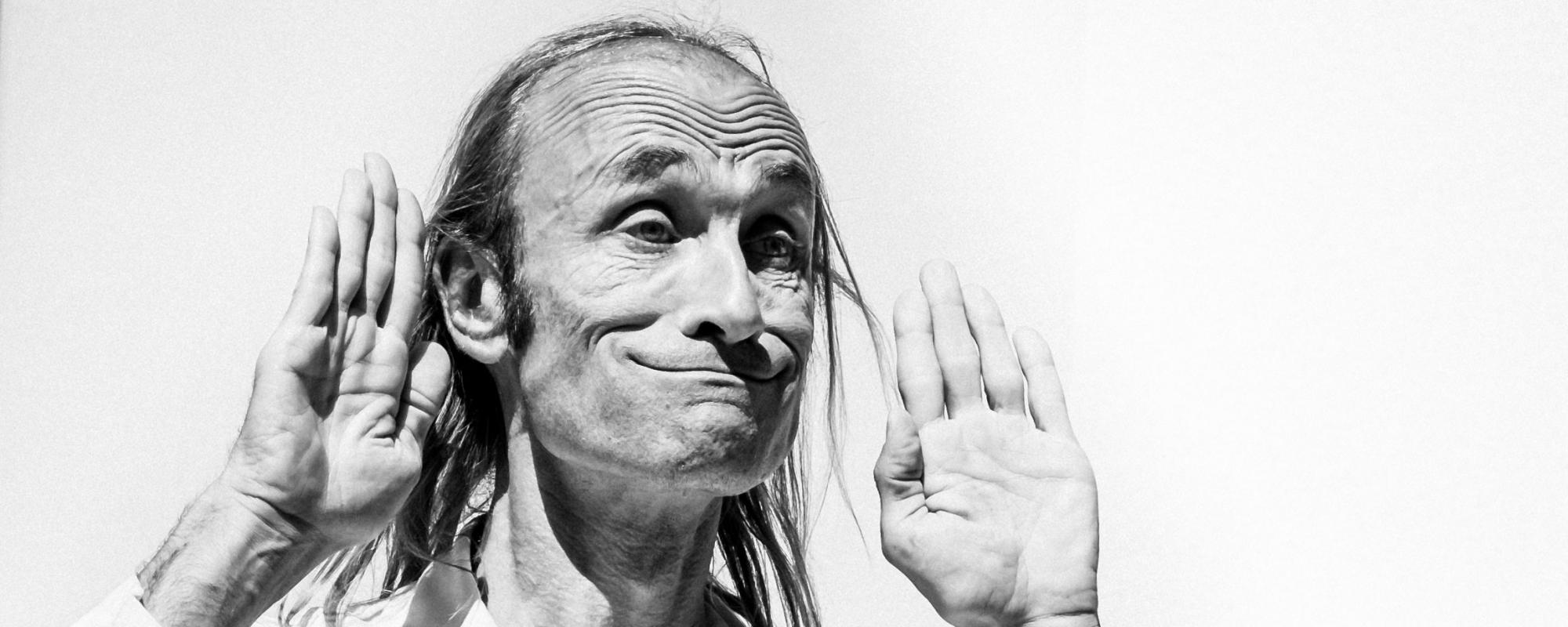 Photo en noir et blanc de Patrick de Valette, sur fond blanc. Il fait une grimace en haussant les sourcils, les mains levées.